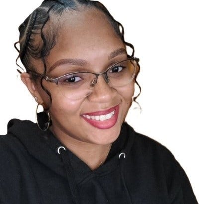 A smiling headshot of Tahina against a white background. She wears glasses, earrings, and a black sweatshirt.