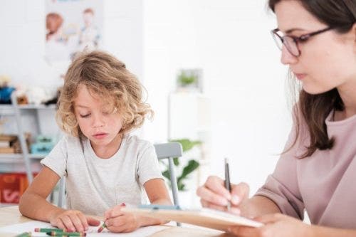 A therapist watches as a child draws pictures.