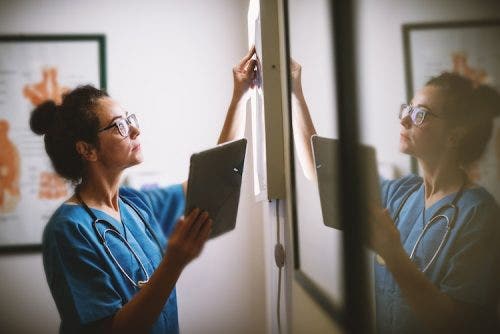 A female nurse in blue scrubs analyzes her patient’s x-ray results.