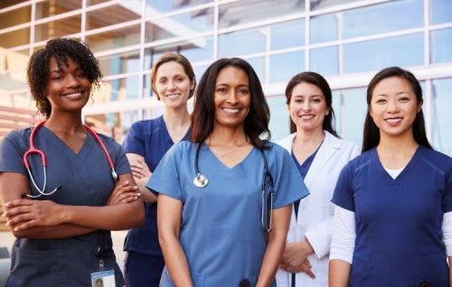 A group of five nurses poses in front of a hospital.