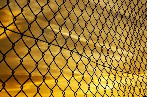 a wire cage fence in front of a yellow sky at sun set