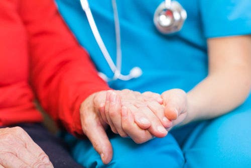 A nurse practitioner holds an elderly patient's hand.