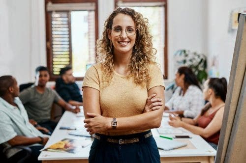 A smiling social services director stands in front of social services workers meeting around a conference table.
