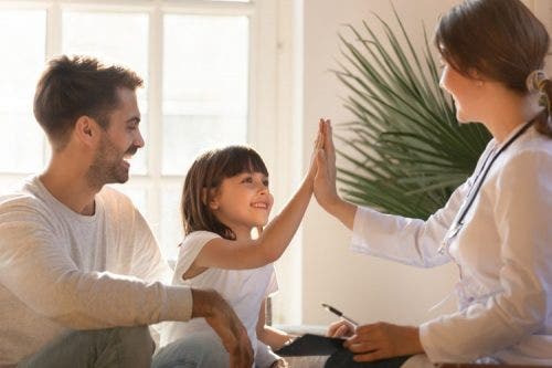A doctor high fives a little girl while her laughing father looks on.
