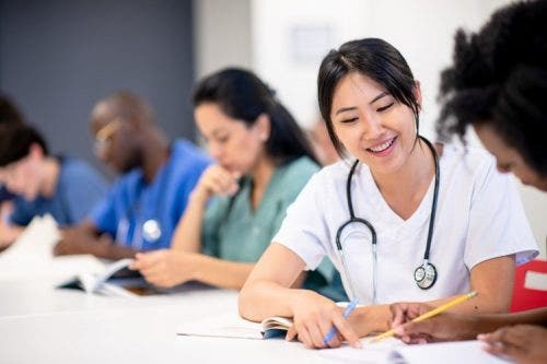 Nursing students in a classroom sitting at a long desk and working together on a project.