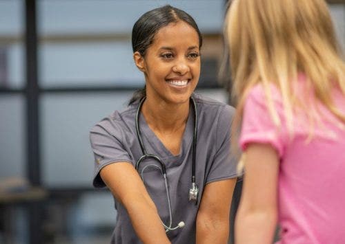 A smiling school nurse meets with a young patient.