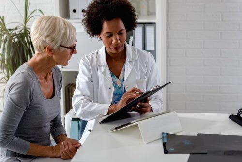 A nurse practitioner holding a clipboard reviews medical records with a patient.