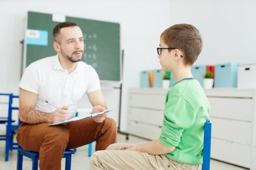 ABA therapist evaluates autistic child patient in a classroom.