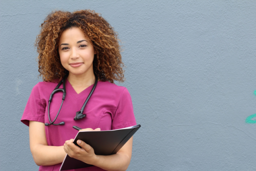 A nurse in purple scrubs poses with a nursing journal.