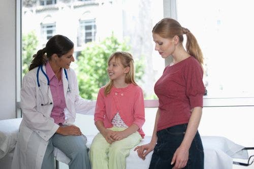 A nurse practitioner interviews a young girl at a clinic as her mother looks on.