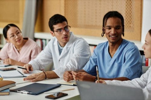 Nursing students seated at a conference table talk to each other.