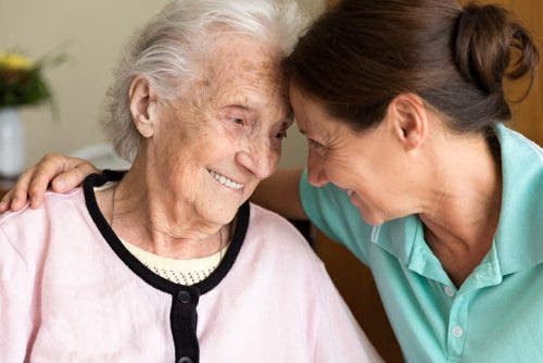 A caregiver and an older adult smile at each other.
