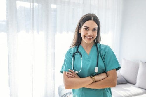 A nurse stands in a room with her arms folded