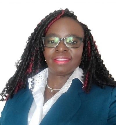 A smiling headshot of Grace against a white background. Grace wears glasses with dark frames and her black curly hair, with streaks of red, is worn down. She is wearing a blue blazer jacket with a white shirt.