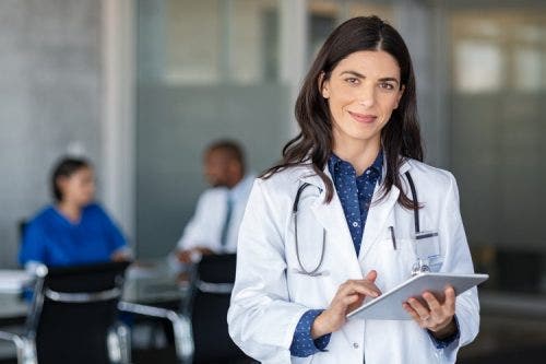 A smiling DNP-prepared nurse practitioner holding a tablet.