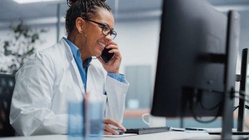 A nurse works in front of a computer monitor while talking on the phone.