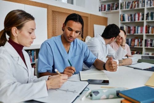 Nurses sit at a table writing in notebooks.