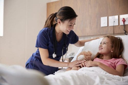 A nurse checks in with a girl lying in a hospital bed.