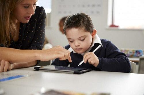 A teacher and a boy use an ACC device while sitting at a desk.