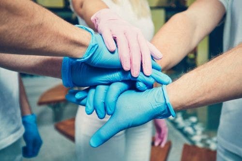 The hands of several nurses are clasped one on top of the other.