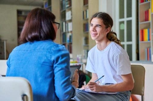 A behavior analyst sits across from a student taking notes in a classroom.