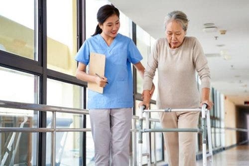 A nursing home nurse assists an older patient using a walker.