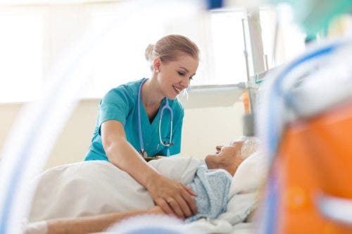 Smiling nurse leaning over and readjusting a patient in a hospital bed.
