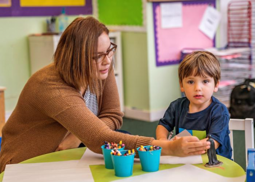 Female school social worker, working with a young male child at a table with an action figure, paper, and crayons.