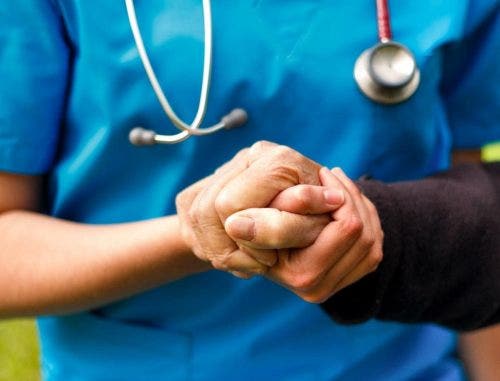 A nurse practitioner holds a patient’s hand.