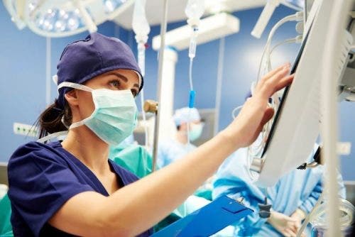 A nurse presses buttons on a digital monitor in a hospital room.