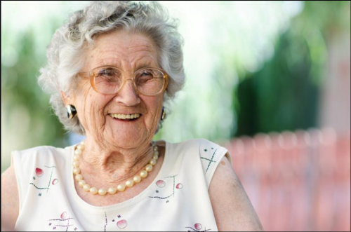 An elderly woman smiles while seated outside.