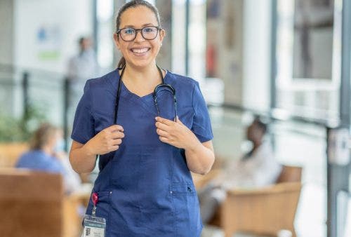 A nurse pauses to smile at the camera in a hospital corridor.