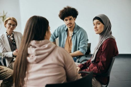 A social worker speaks with a group of people seated in a circle.