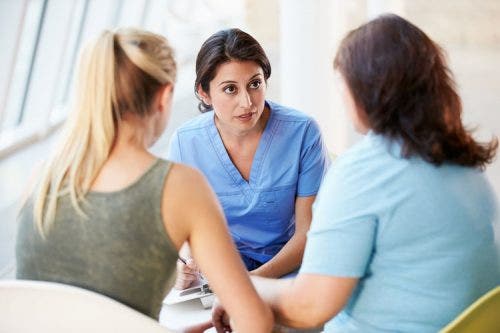 A nurse practitioner in scrubs meeting with a mother and daughter in a clinical setting.