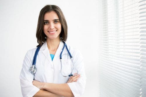 Smiling nurse in a lab coat and stethoscope standing with arms crossed.