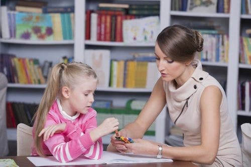 An ABA therapist hands crayons to a child.