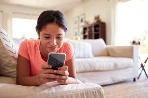 A teenager lying on the couch and looking at her smartphone.