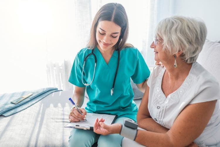 A nurse checks a patient’s blood pressure while writing on a medical chart.
