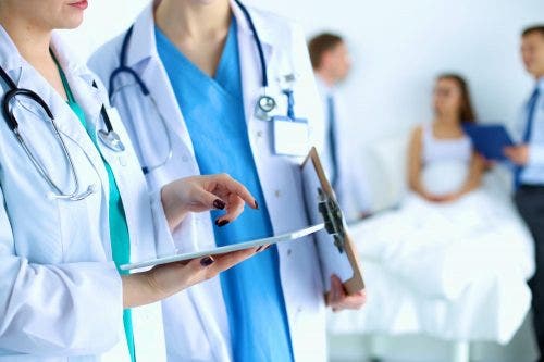 Two nurse practitioners use a tablet to review patient data in an exam room.