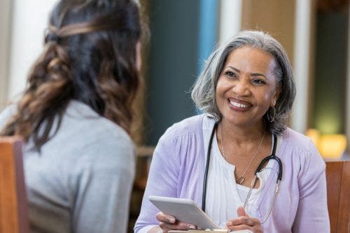 A nurse smiles while taking notes during a patient interview.