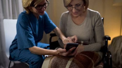 A nurse helps an elderly patient use an app to monitor health.