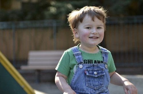 A little boy in overalls smiles at the camera.