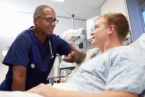 A nurse practitioner speaks with a patient lying in a hospital bed.